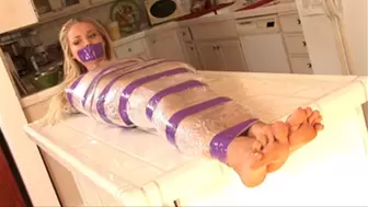 Delicate blonde nude Staci Carr stood wrapped with clear plastic and purple tape, then lay on a kitchen island!